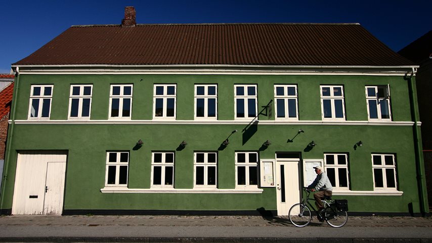 Mand cykler på gaden foran grøn bolig