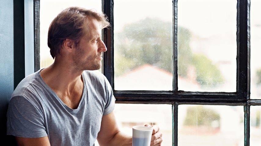 Mand med kaffe sidder ved vindue